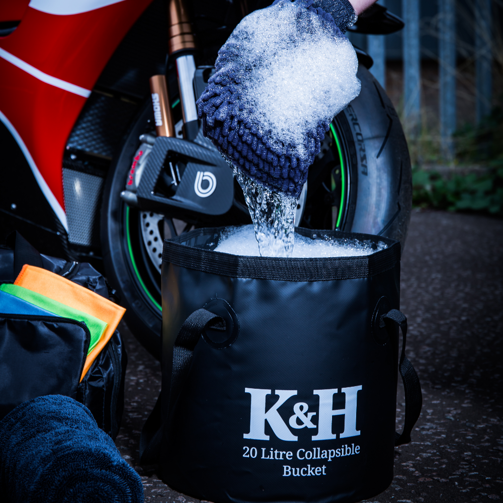 Person cleaning a motorcycle with a K&H collapsible bucket and sponge.