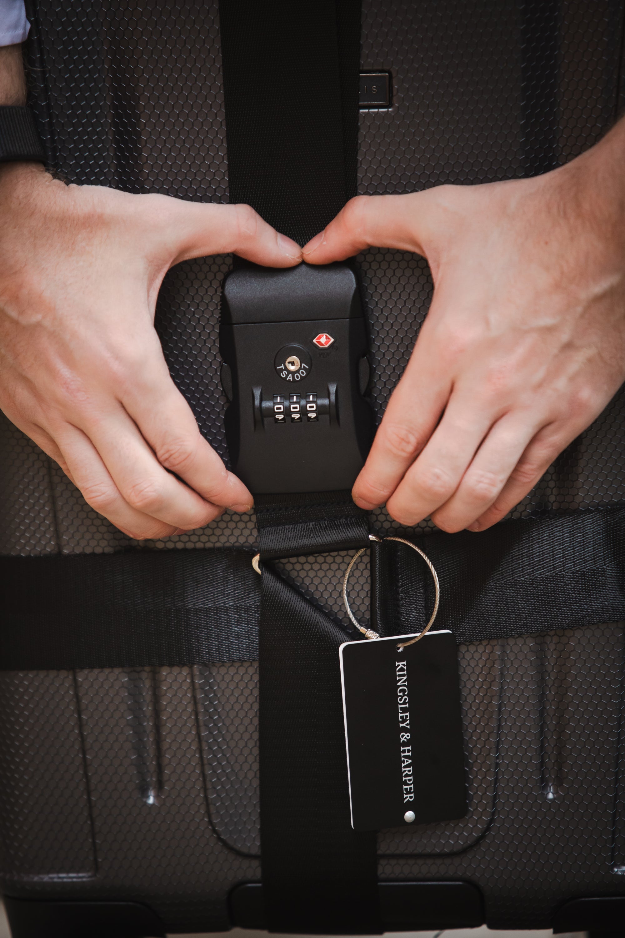 Black combination lock with three dials and a red logo, attached to a suitcase strap